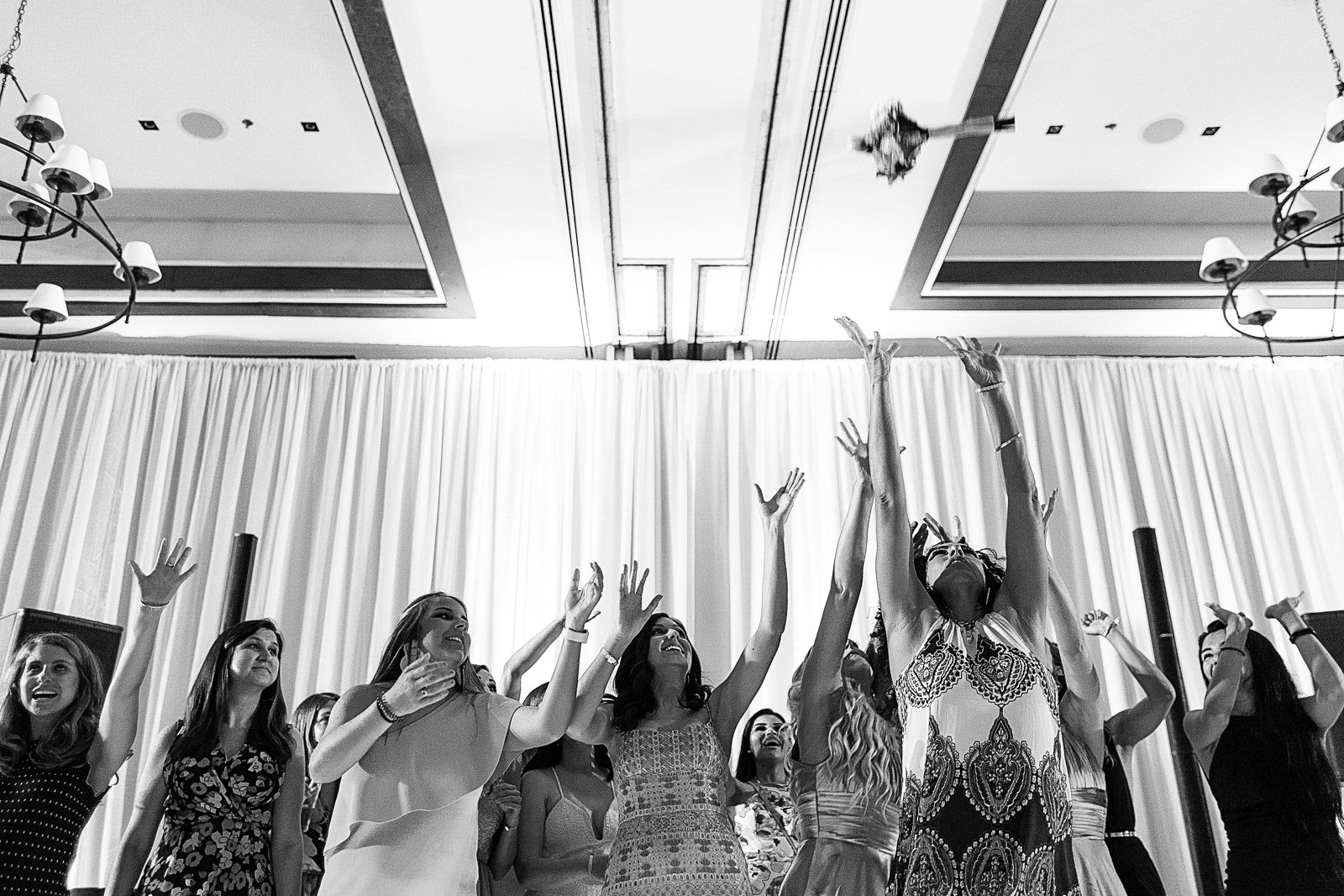 Bouquet tossed in the air, wedding guests females about to catch it.