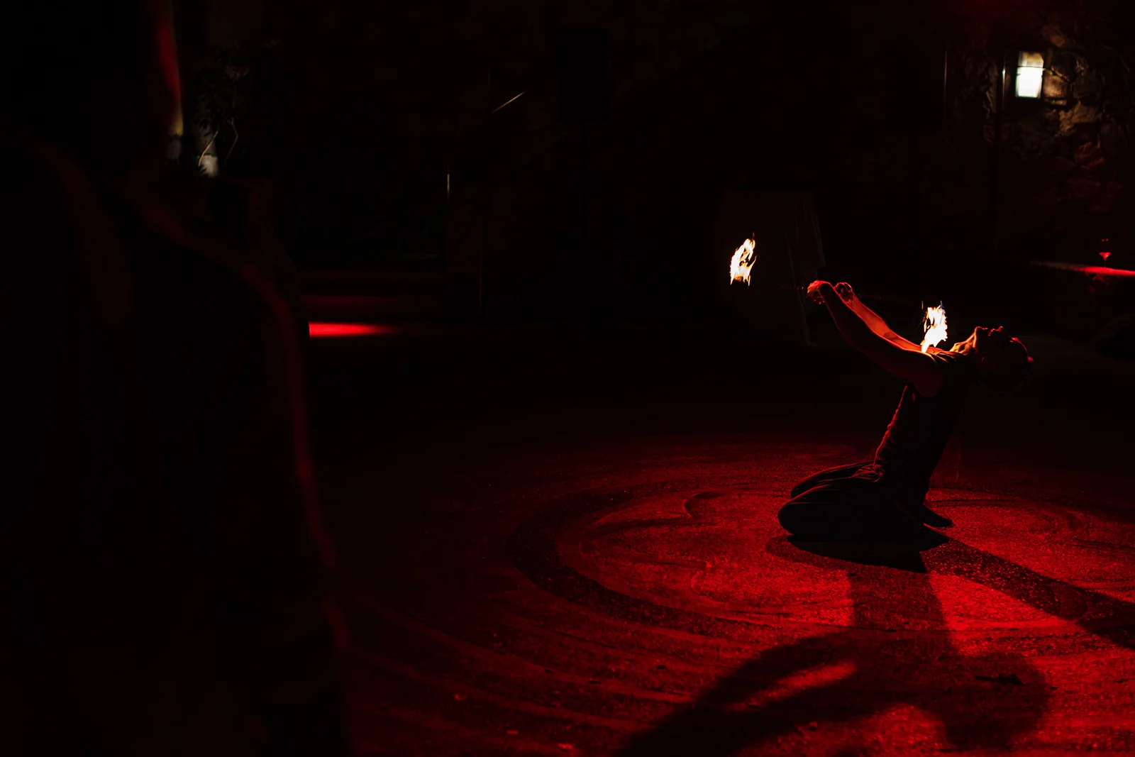Firedancer plays with fire while kneeling down, during the destination wedding reception.