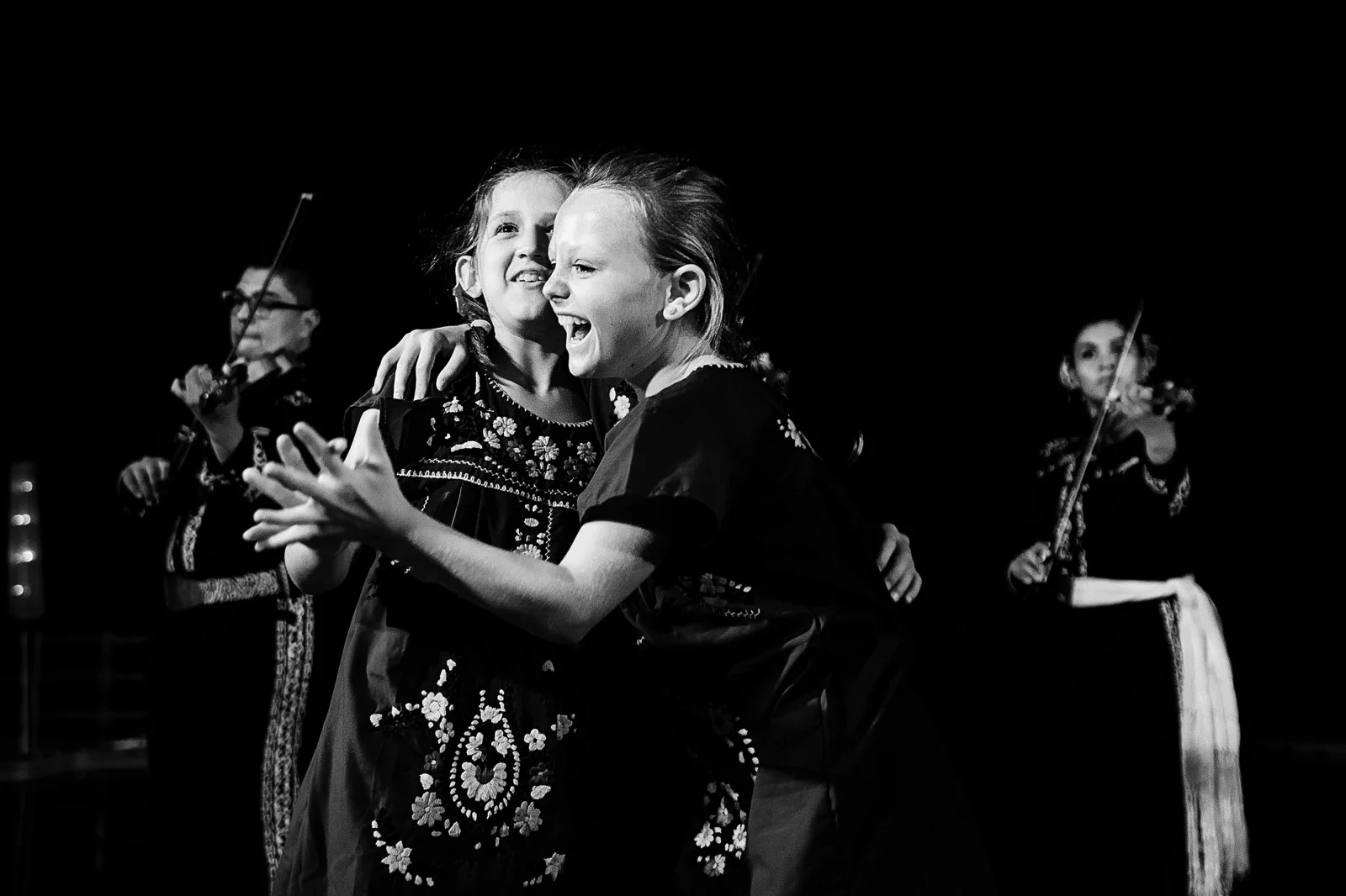 Flower girls laugh and have fun while mariachi band plays behind them