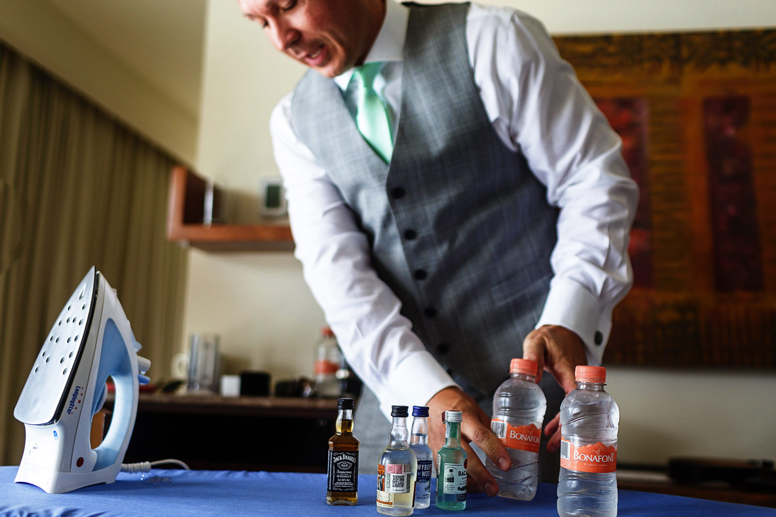 The groom takes all the mini-bottles of alcohol and place them over the ironing table
