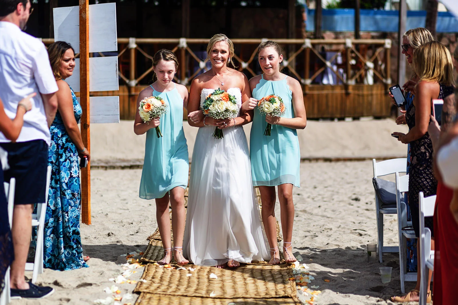 Bride and daughters bridesmaids walking down the aisle for the ceremony on the beach
