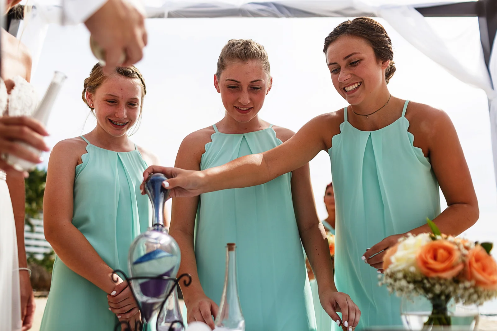 Daughters of the groom and bride filling the container during the sand ceremony on the beach of Mexico