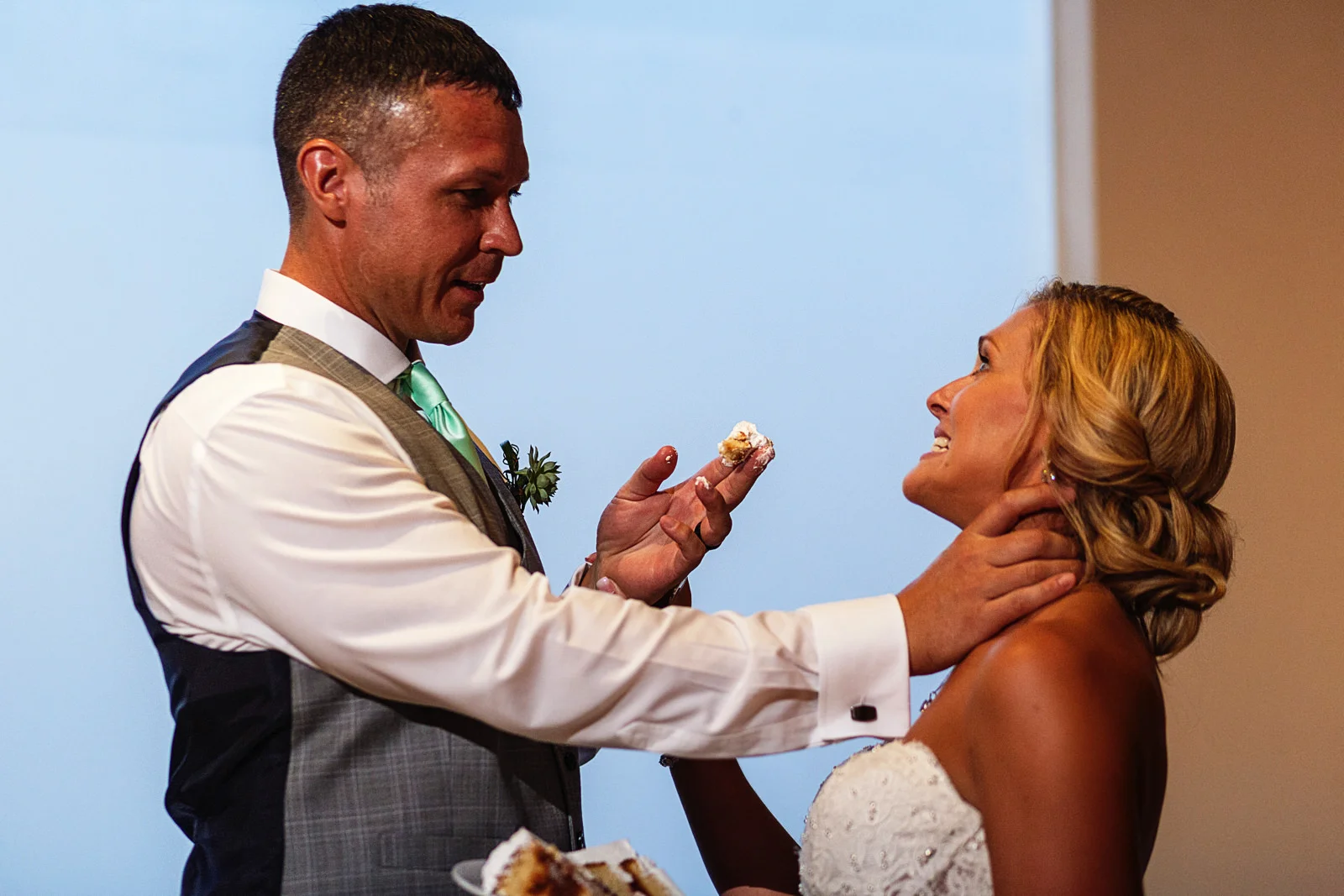 Groom grabs the bride by the neck and try to feed her with wedding cake