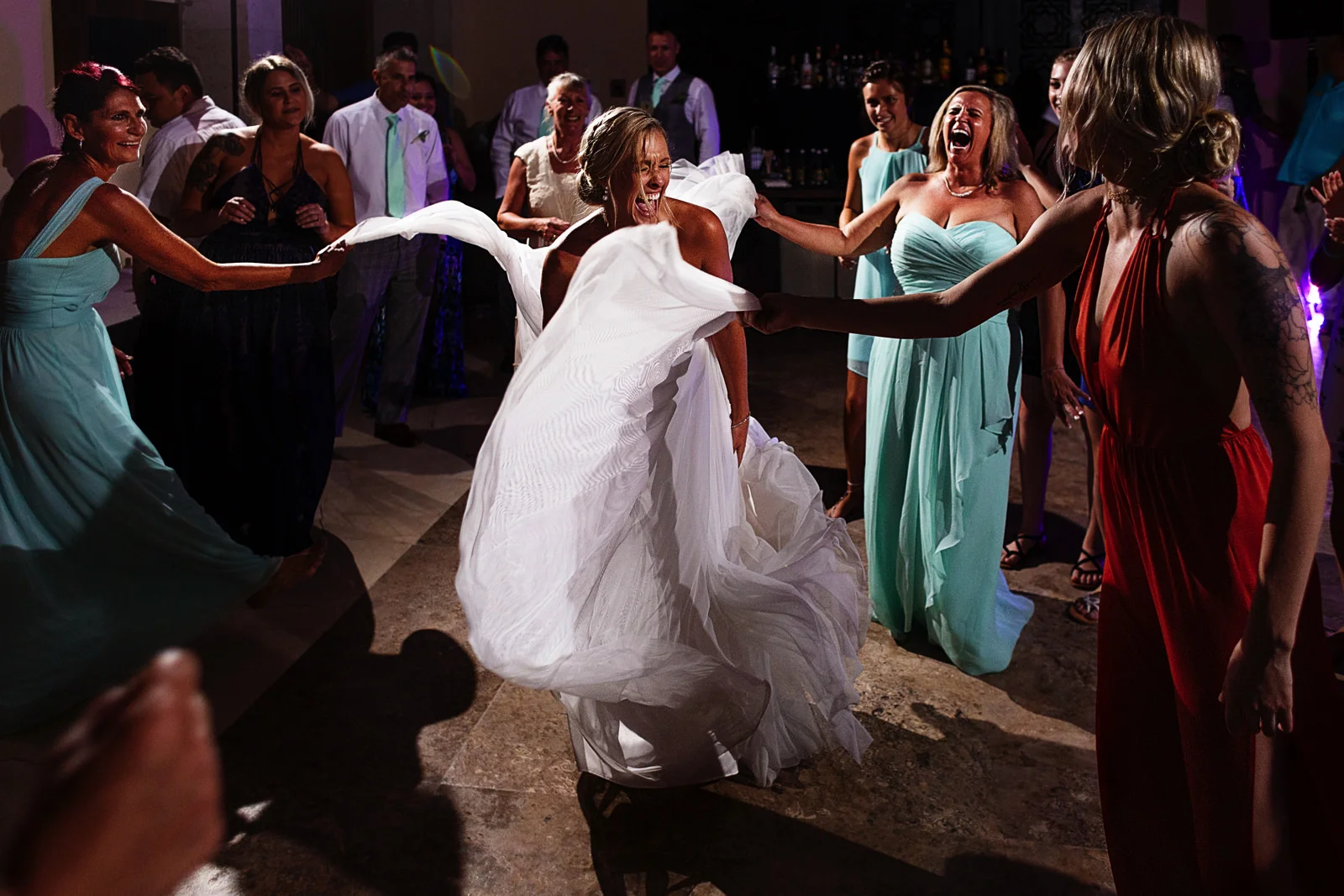 Wedding guests hold and lift the bride's dress in the dance floor