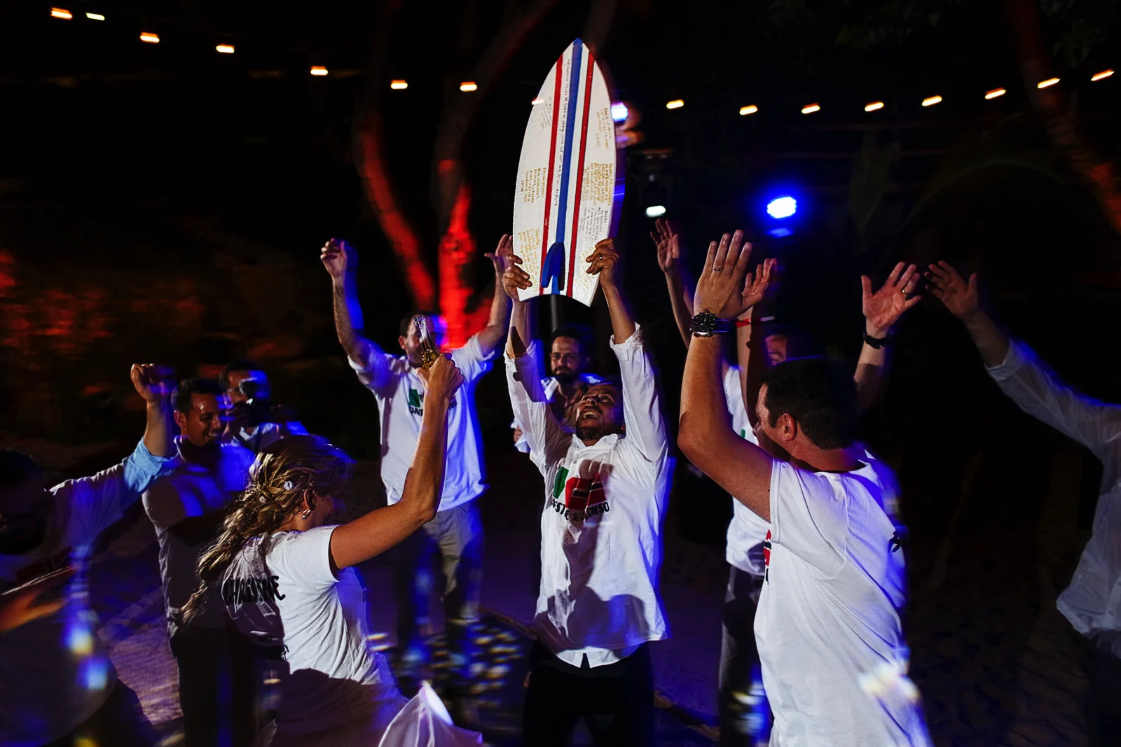 Groom raises a signed surf board as everybody jumps around the happy couple