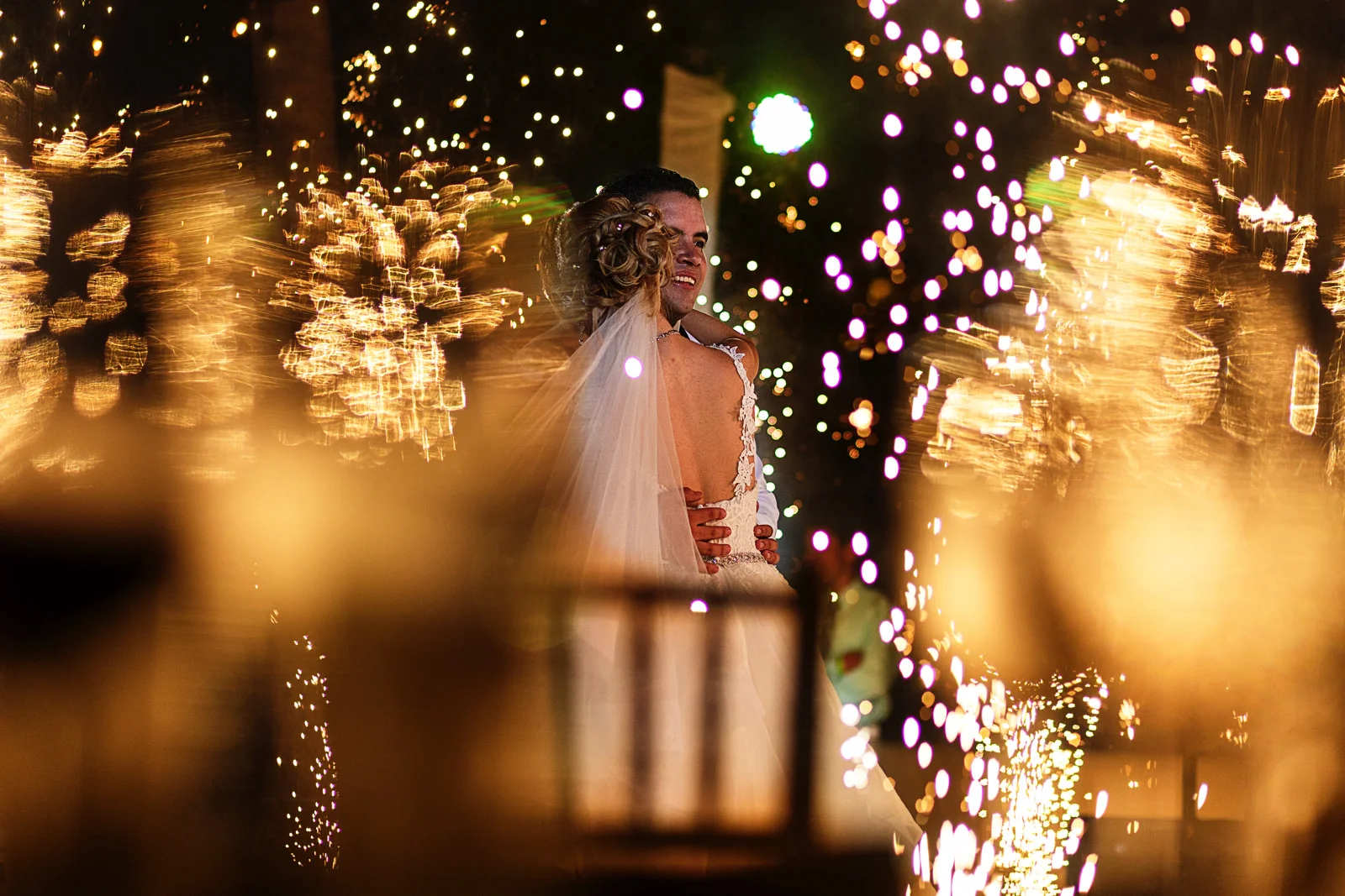 Bride and groom on their first dance thru champagne glasses as the floor sparklers explode