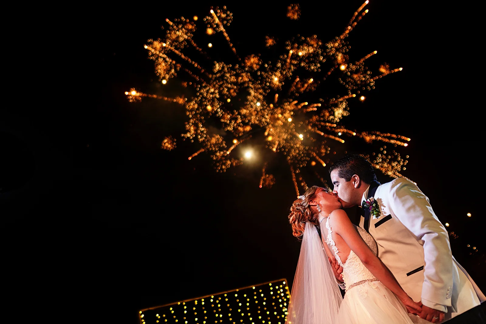 Bride and groom kiss under the fireworks at the end of their first dance as married couple