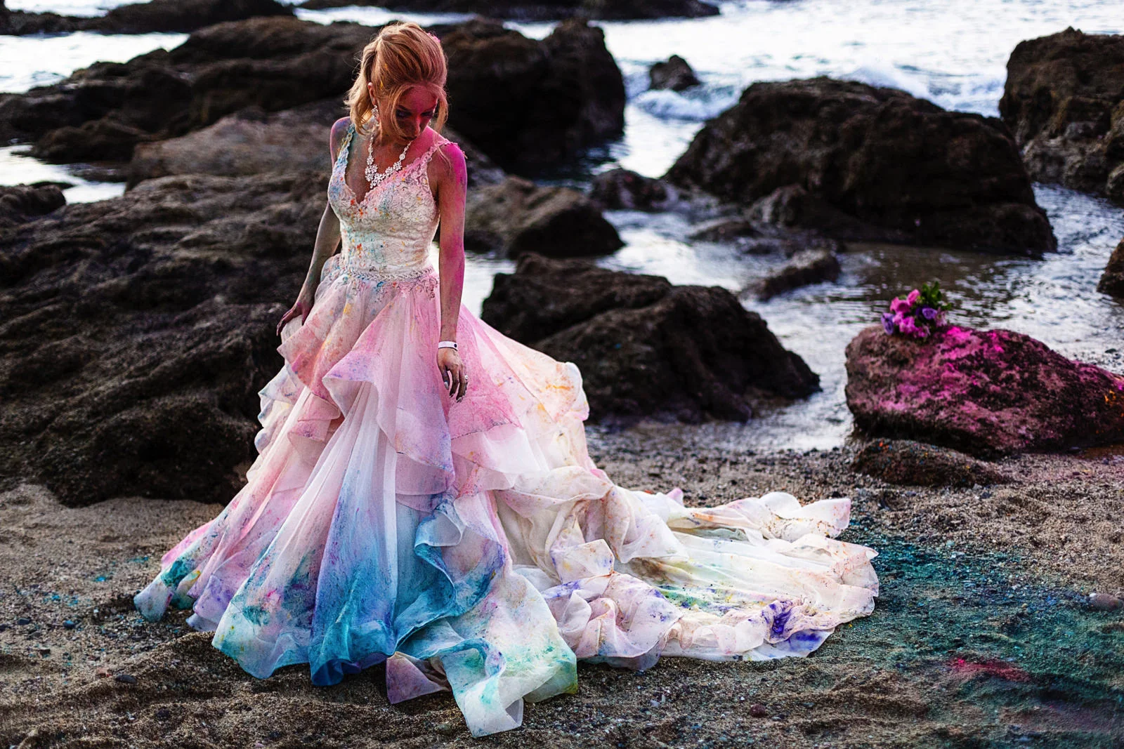Bride with colorful wedding dress covered in holy powder standing near the ocean