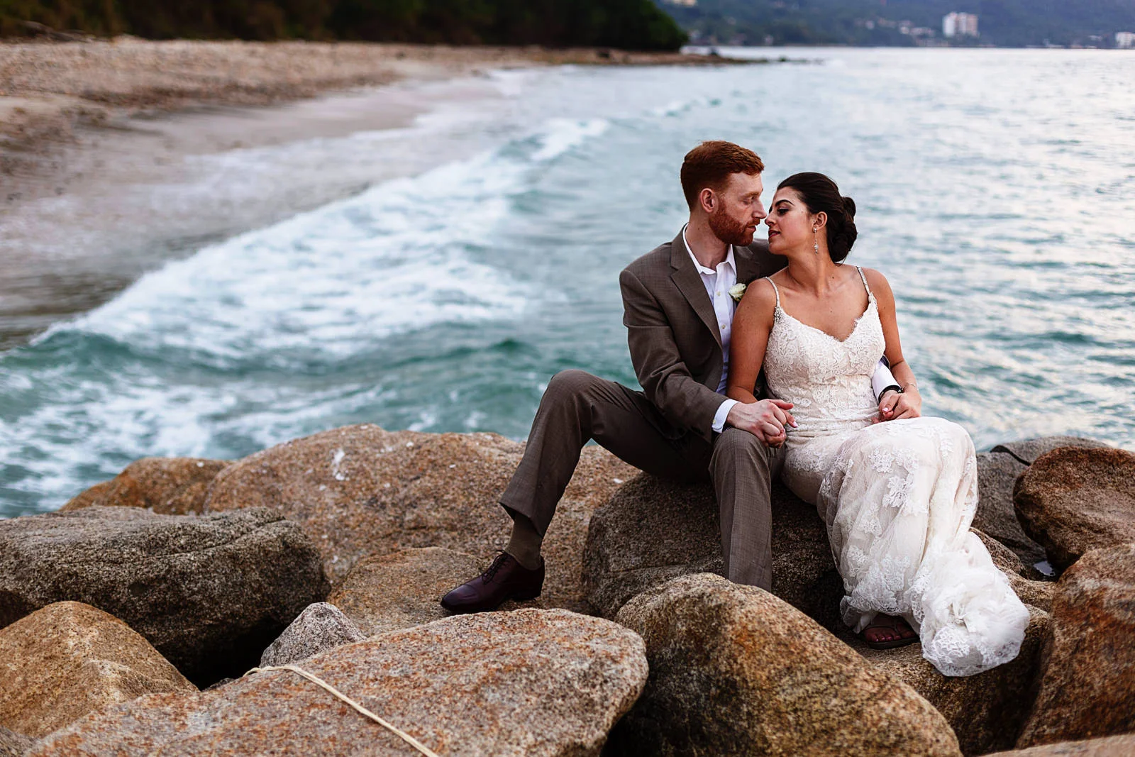 Recently married couple sitting in the rocks inside the pacific ocean with waves passing them behind.