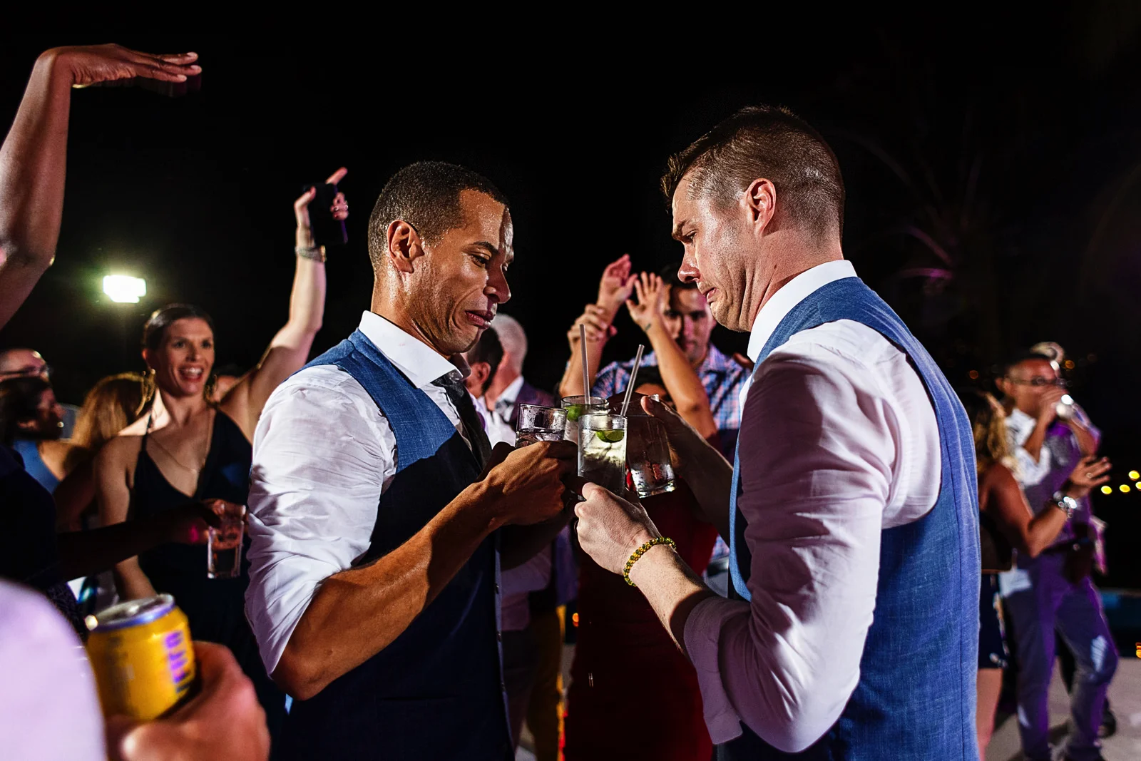 Grooms make funny faces as they put their drinks together in the dancefloor