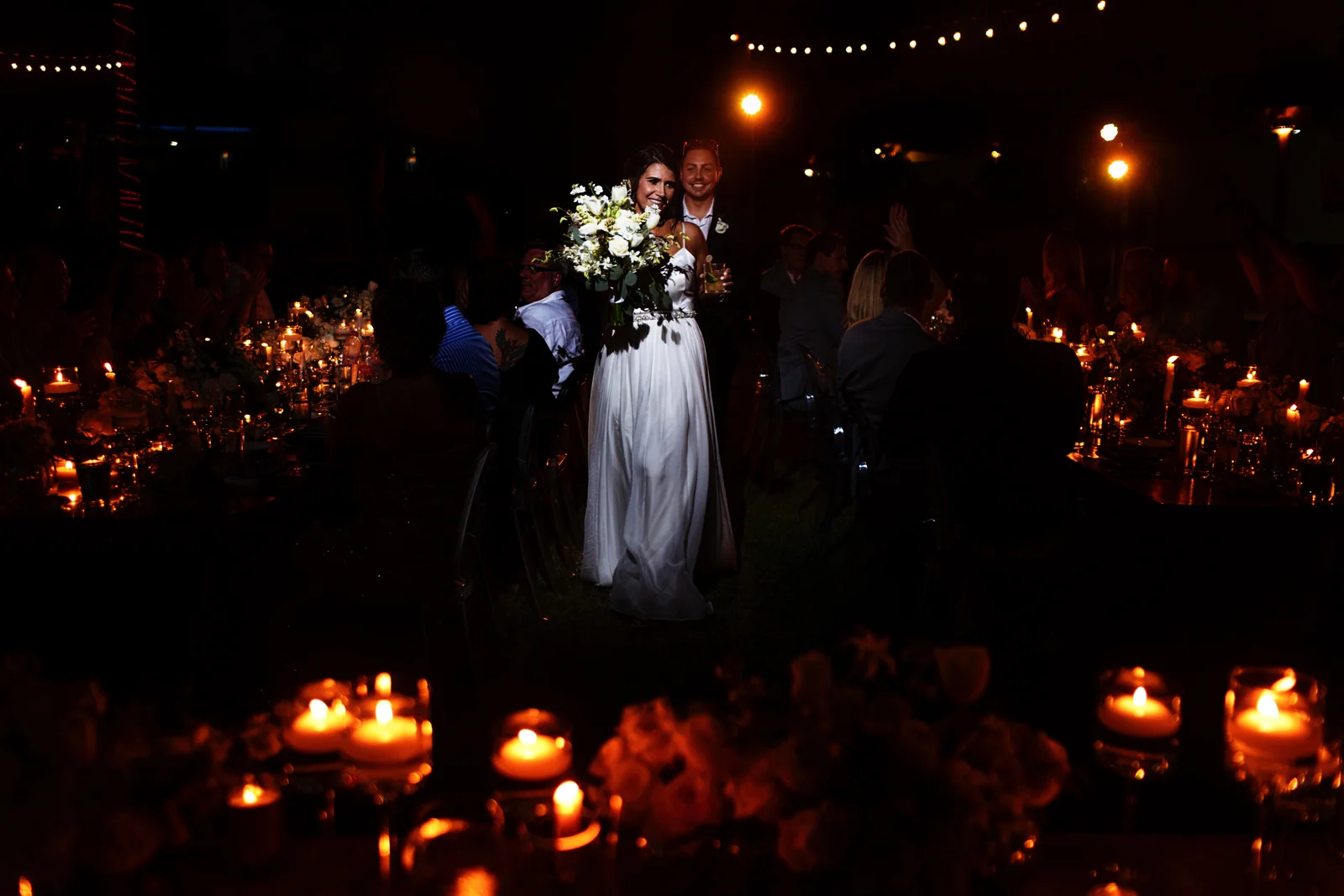 Bride and groom entrance into the reception between the dinning tables filled with candles