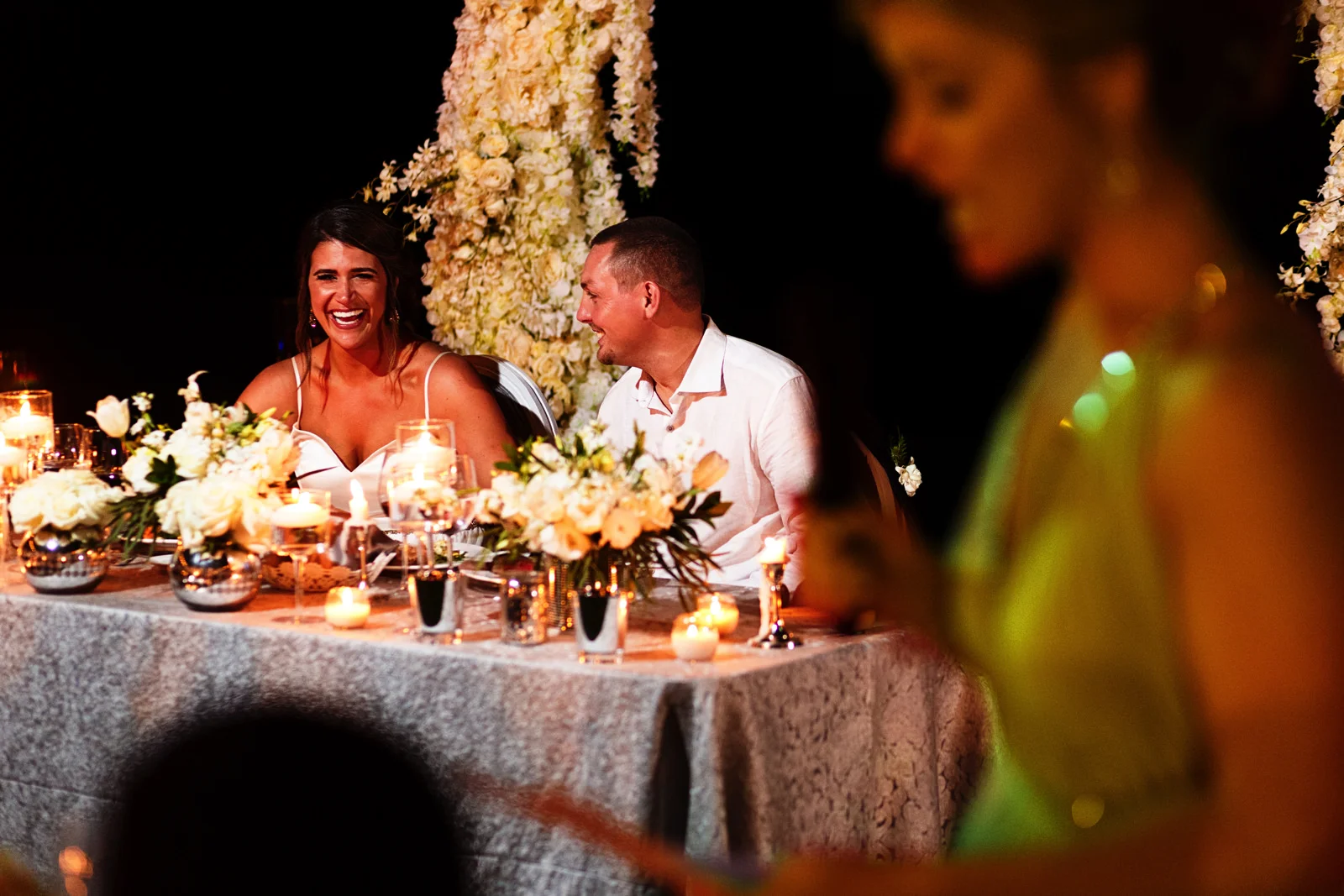 Bride and groom laugh during the matron-of-honor's speech