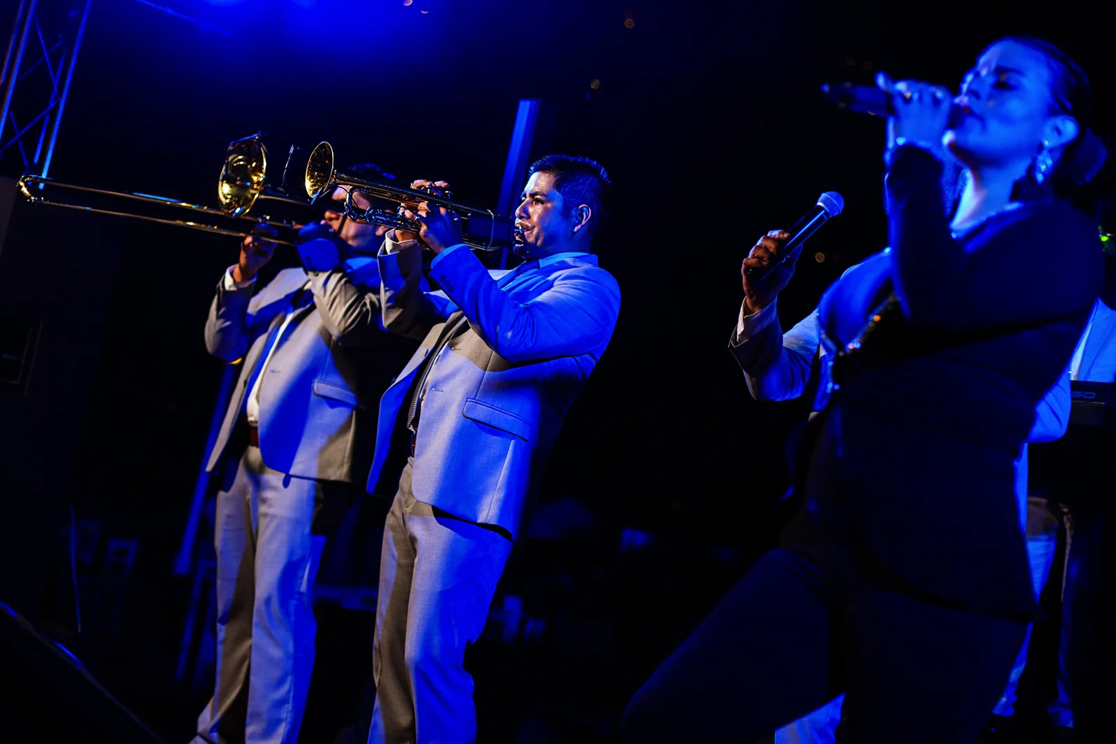 Brass section of he music band on stage with blue lights and female singer in the foreground