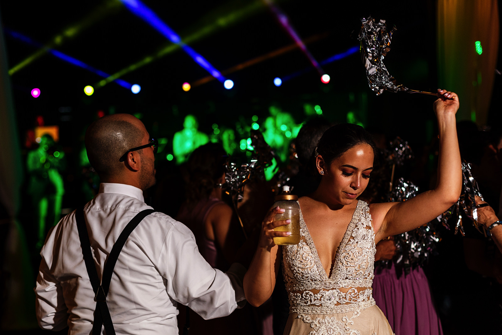 Bride dancing with brother-in-law holding a drink and waving a stick with silver feathers