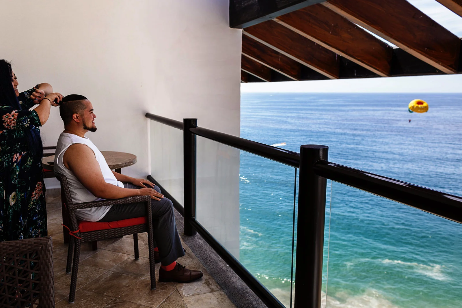 Groom getting hi hair done as a parachute is flying over the ocean