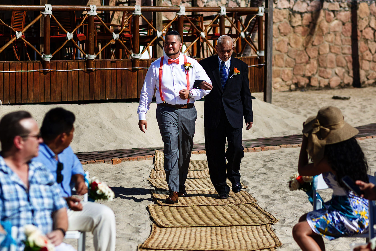 Groom walks down the aisle with the father of the bride on the beach