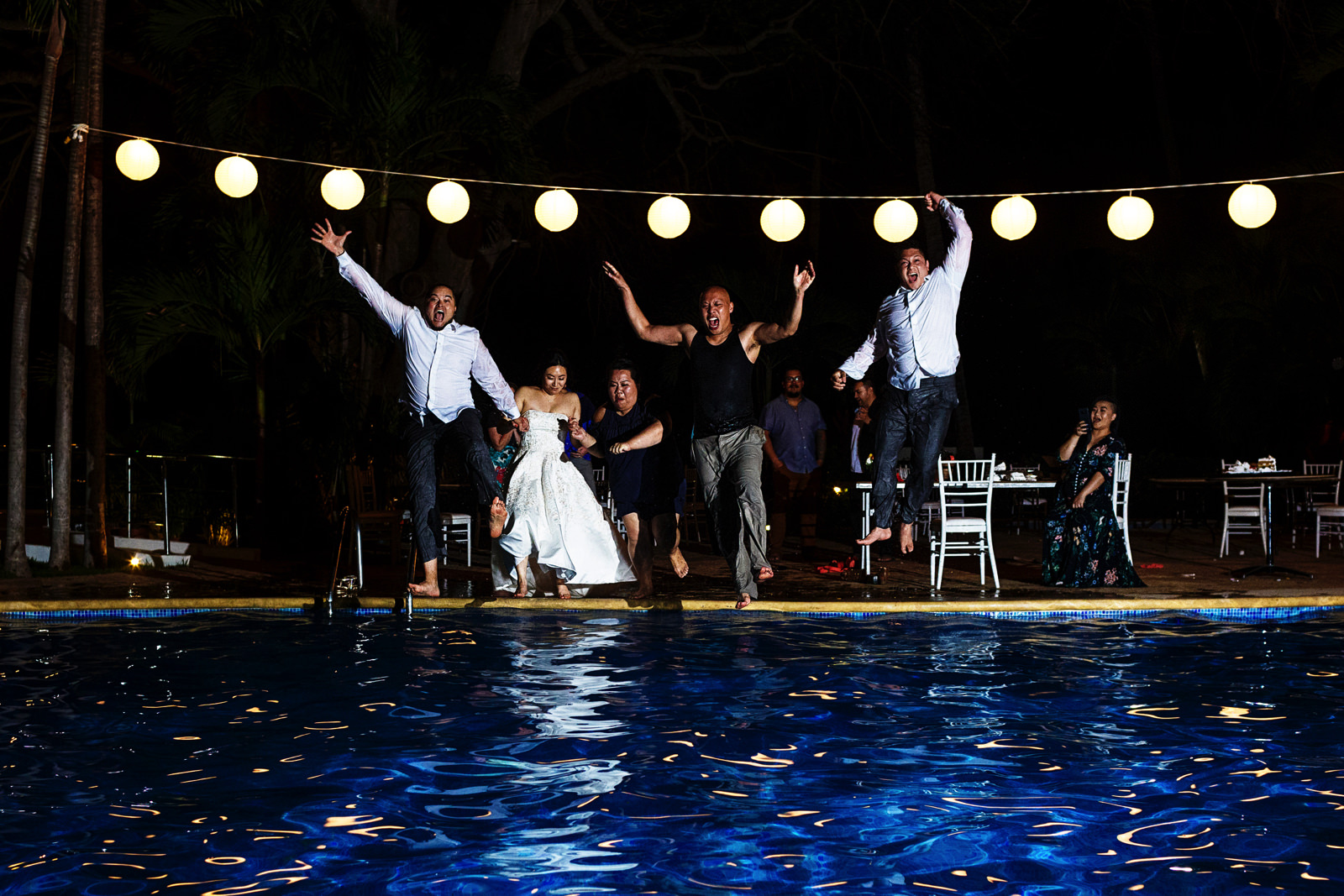 Groom and bride jump into the hotel pool among other wedding guests