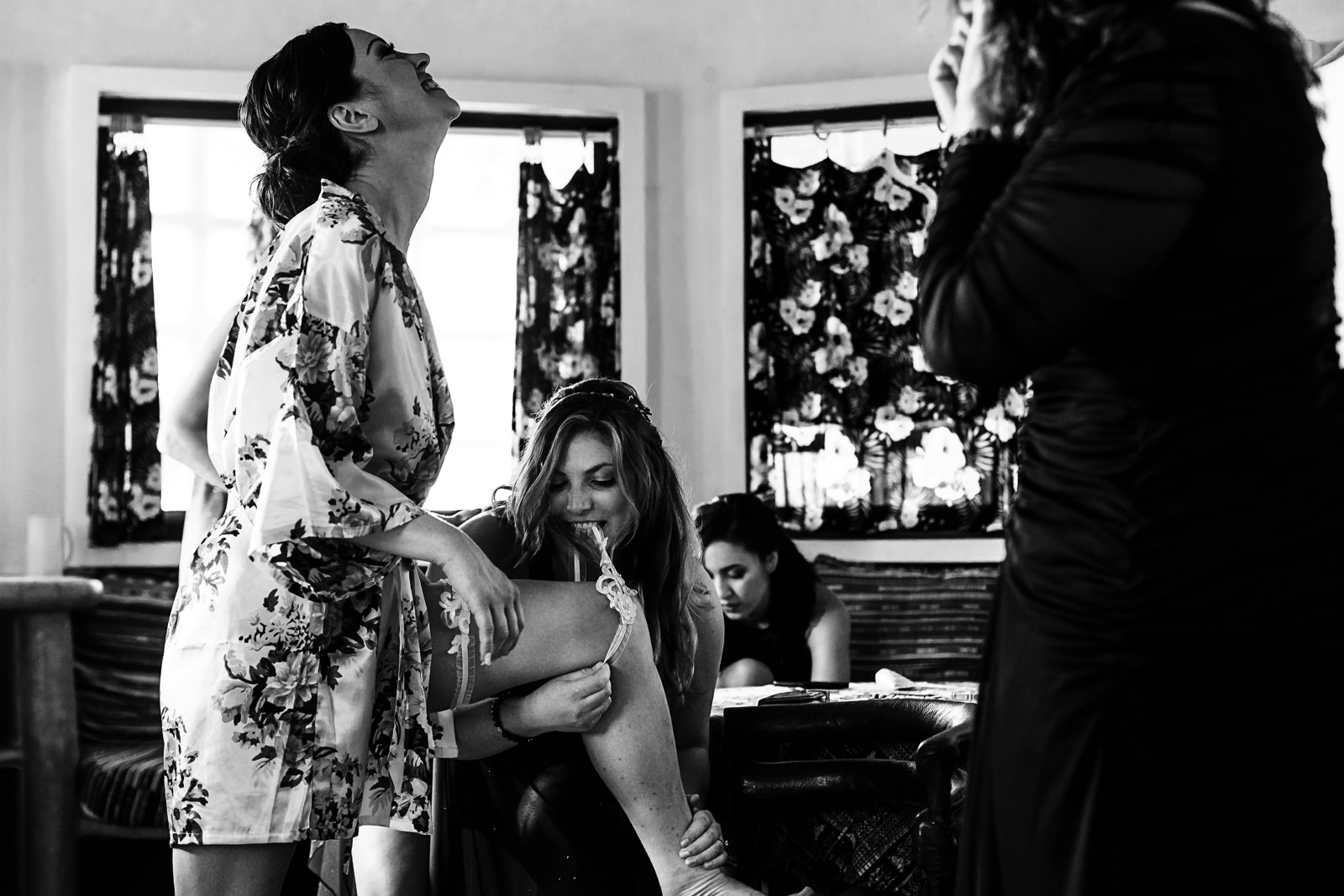 Bridesmaid putting the garter on the bride’s leg with her teeth