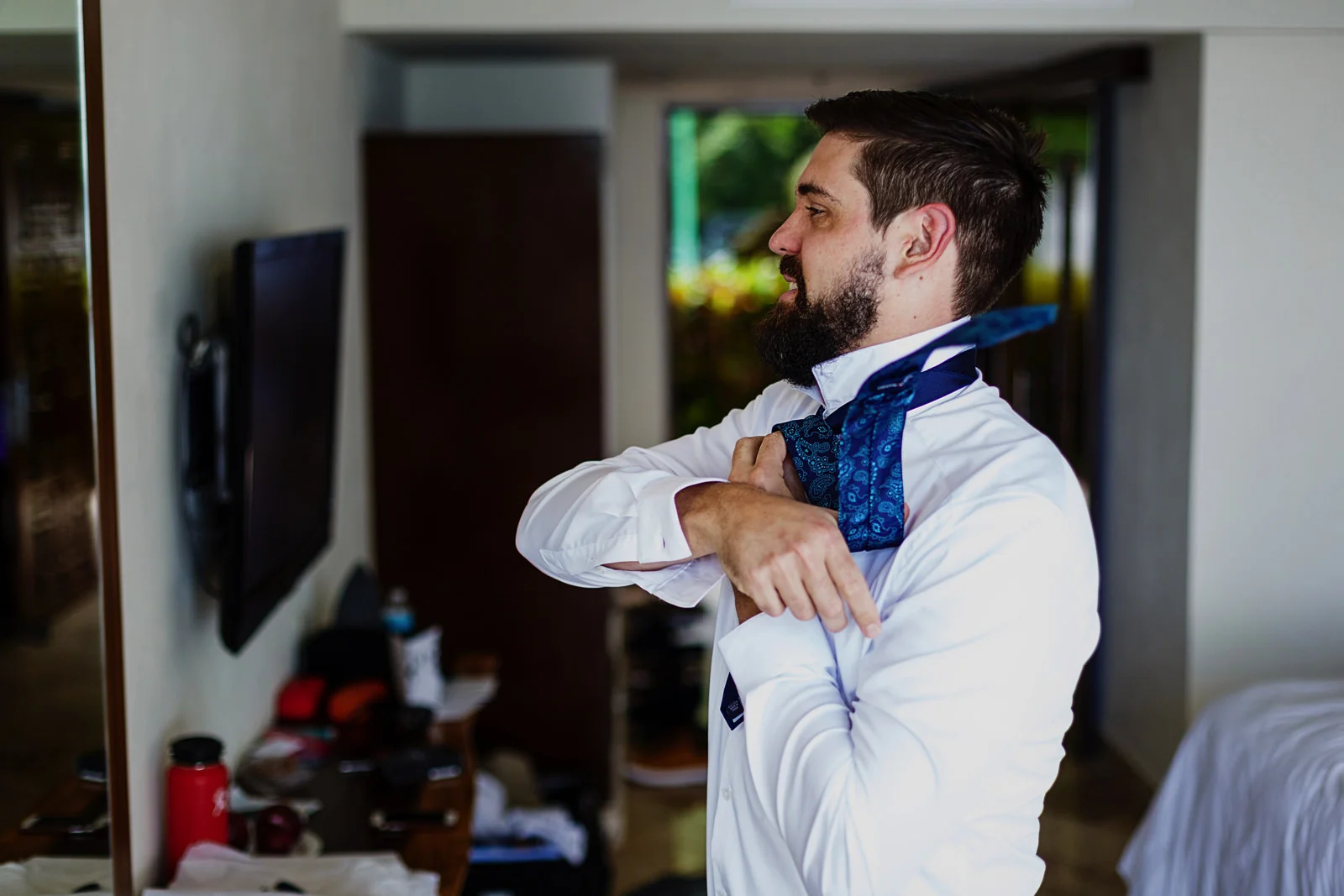 Groom looking at himself in the mirror while doing his tie knot.