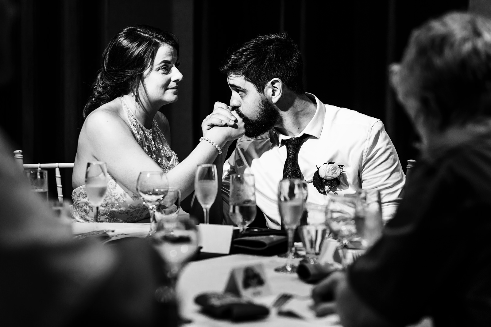 Groom kisses his bride’s hand during the speeches at the dinner table.