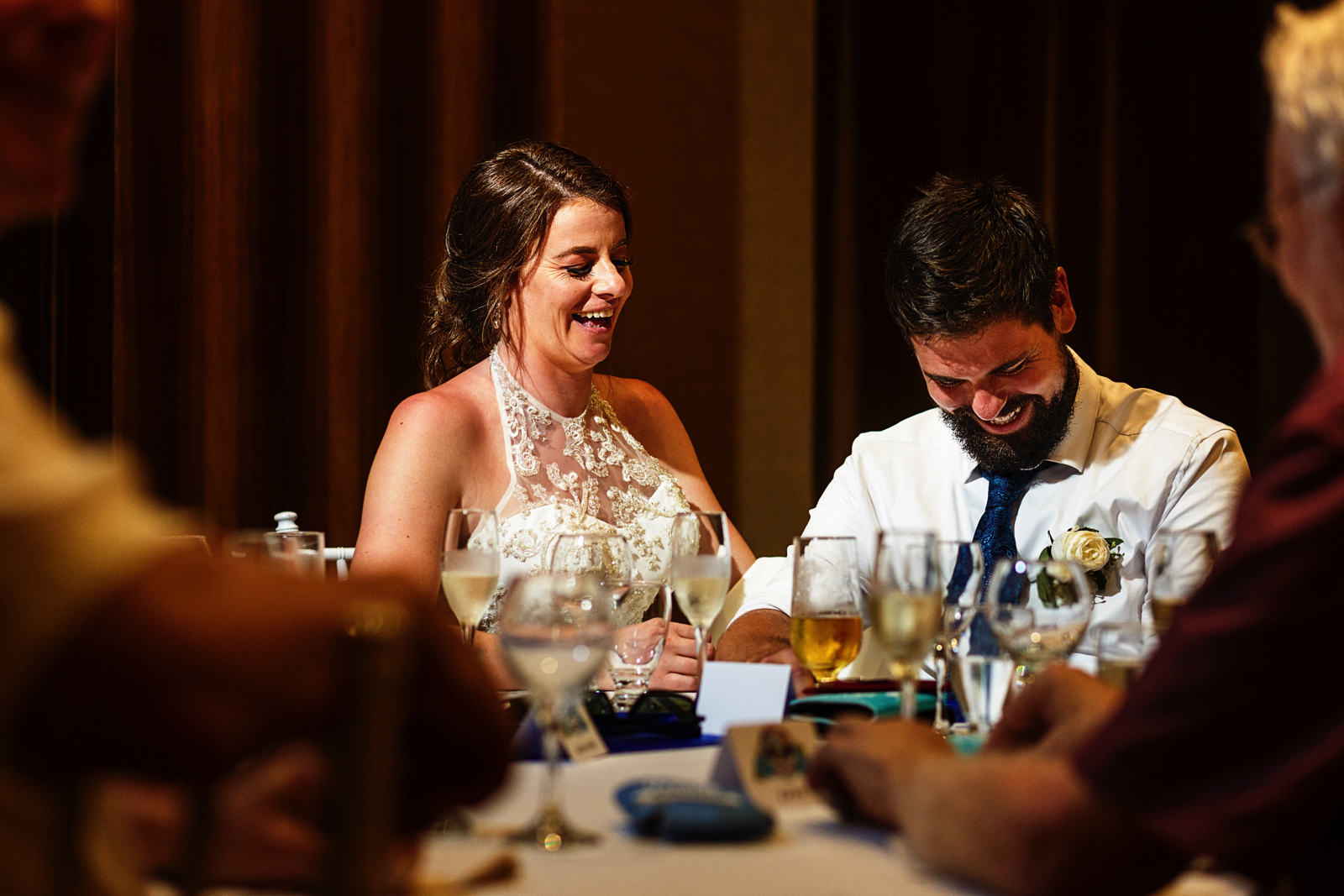 Groom and bride laughing during the speeches at the dinner table.