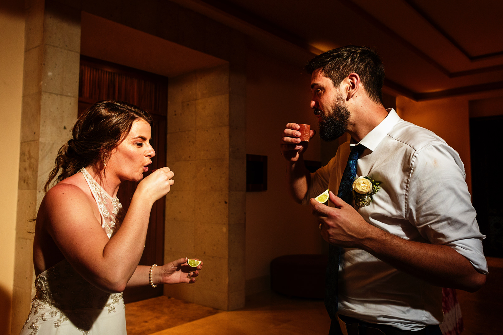 Groom and bride about to drink a tequila shot, while holding  a slice of lime on the other hand.