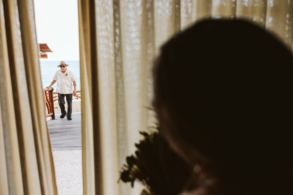 Father of the bride arriving to the room as the bride peeks outside