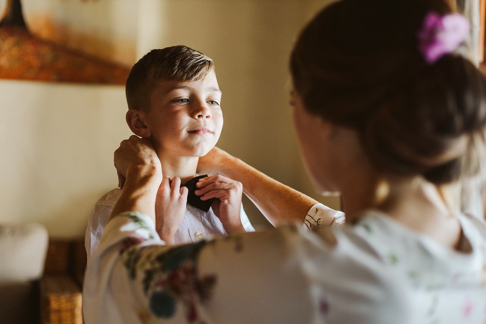 Bride helps ring bearer to put on his bow tie during getting ready at Hotel Playa Fiesta
