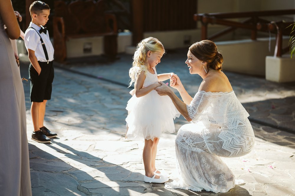 Bride and flower girl share a moment before portraits, in the parking lot outside Hotel Playa Fiesta