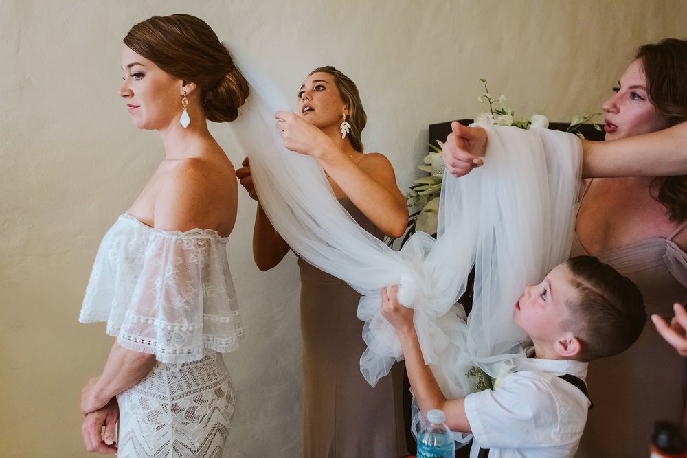 Bridesmaids and ring bearer help the bride to put on her long veil, before heading to the wedding ceremony