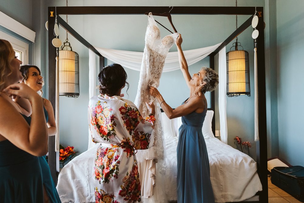Mother of the bride helps bringing down the wedding dress from hanging on the bed