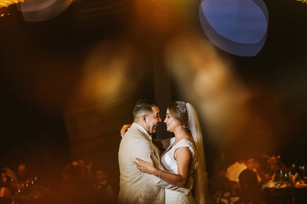 Bride and groom first dance, viewed between two wine glasses