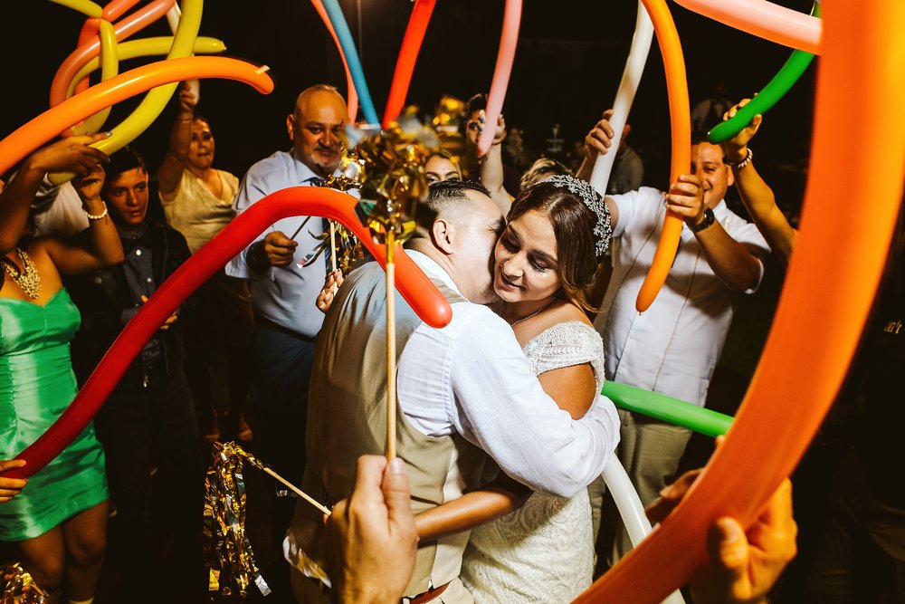 Wedding guests dancing around the groom and bride with long balloons