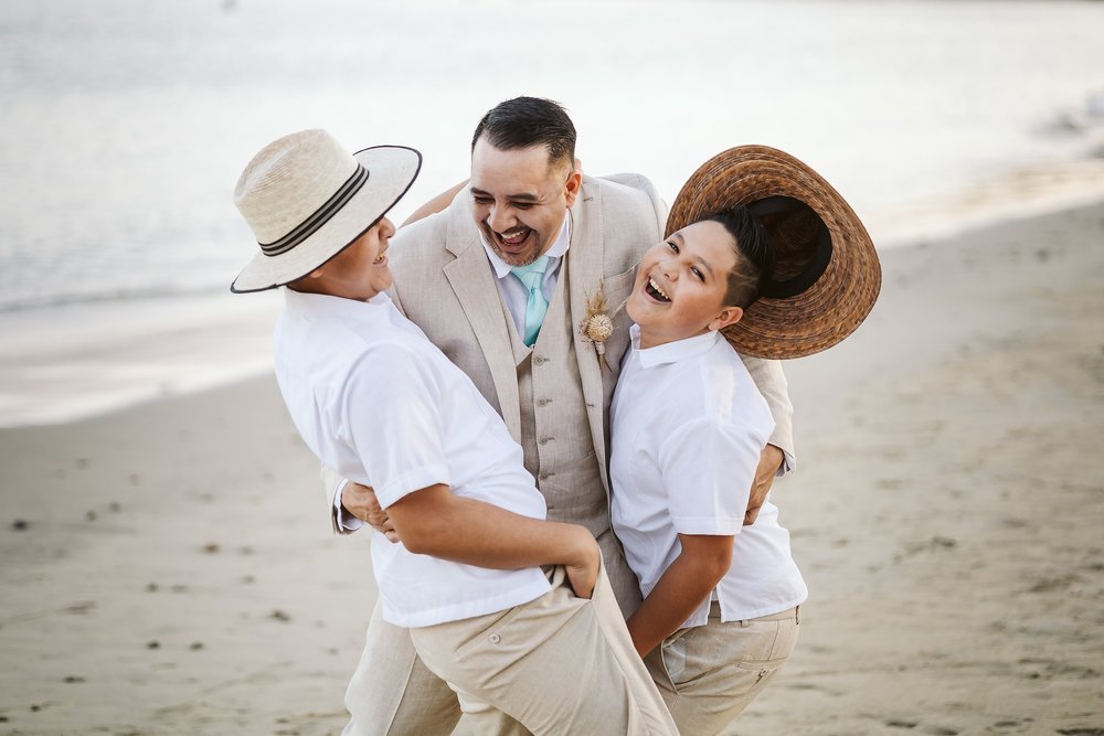 Groom plays and have fun during portraits with their sons on the beach