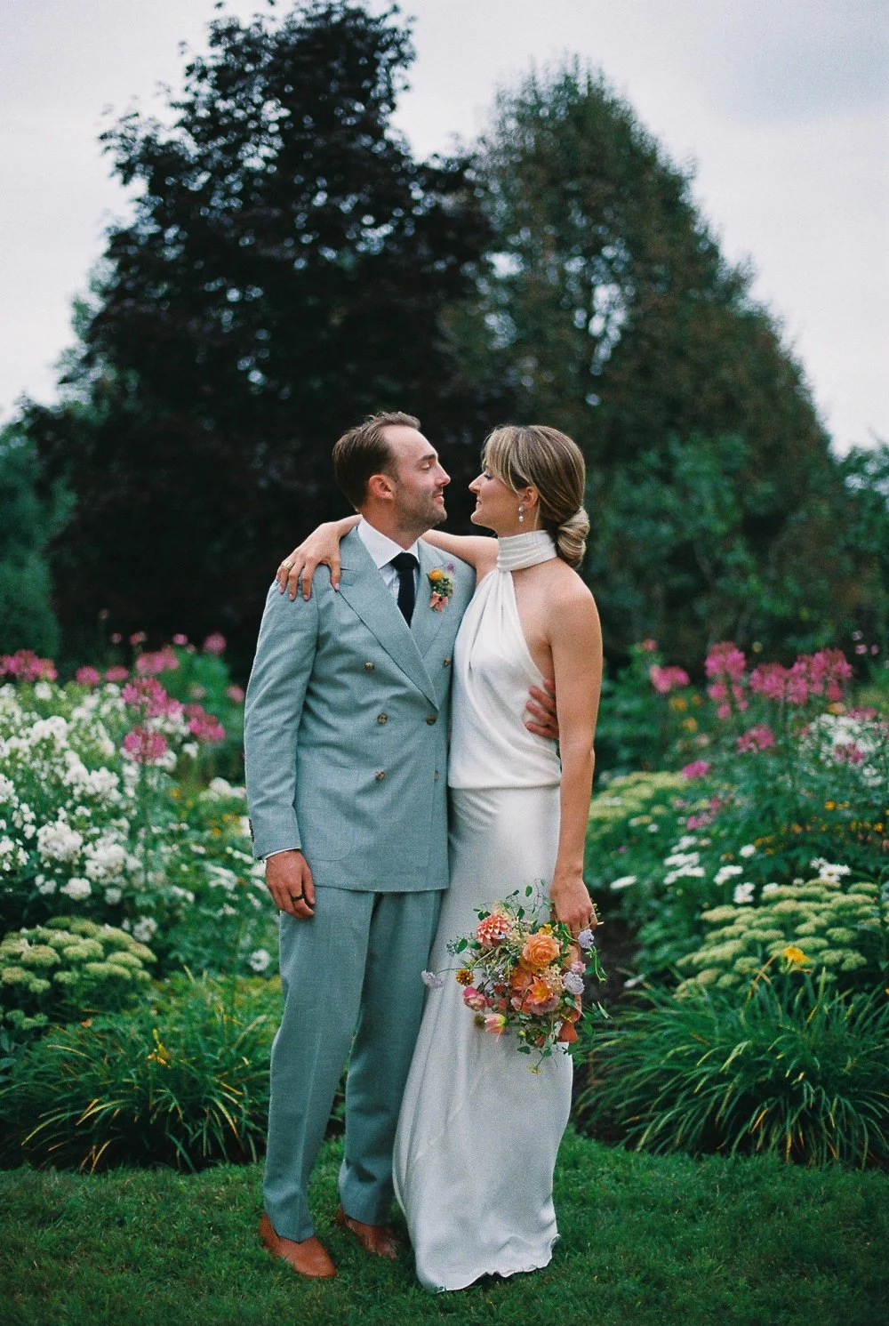 A bride and groom embracing in a garden with blooming flowers, standing close and gazing at each other during their wedding.