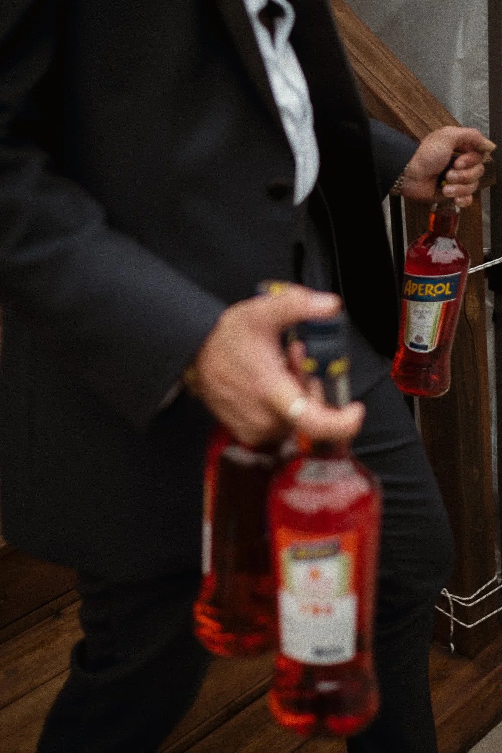 Bestman in a black suit holding multiple bottles of Aperol, an Italian apéritif during a wedding.