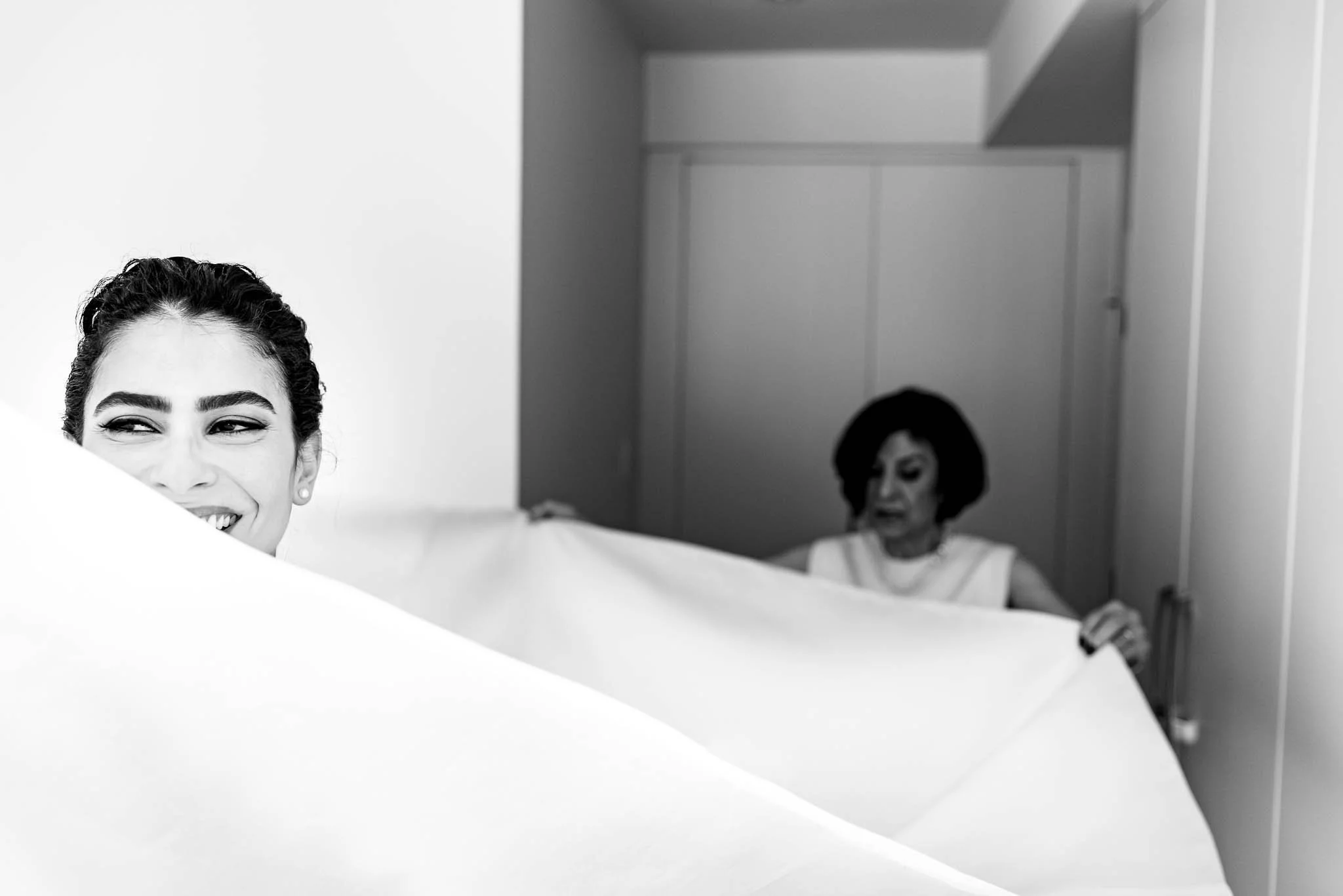 Two women holding a large sheet of paper, one smiling and the other looking down. The woman on the left has dark hair in an updo, and the woman on the right has short dark hair.