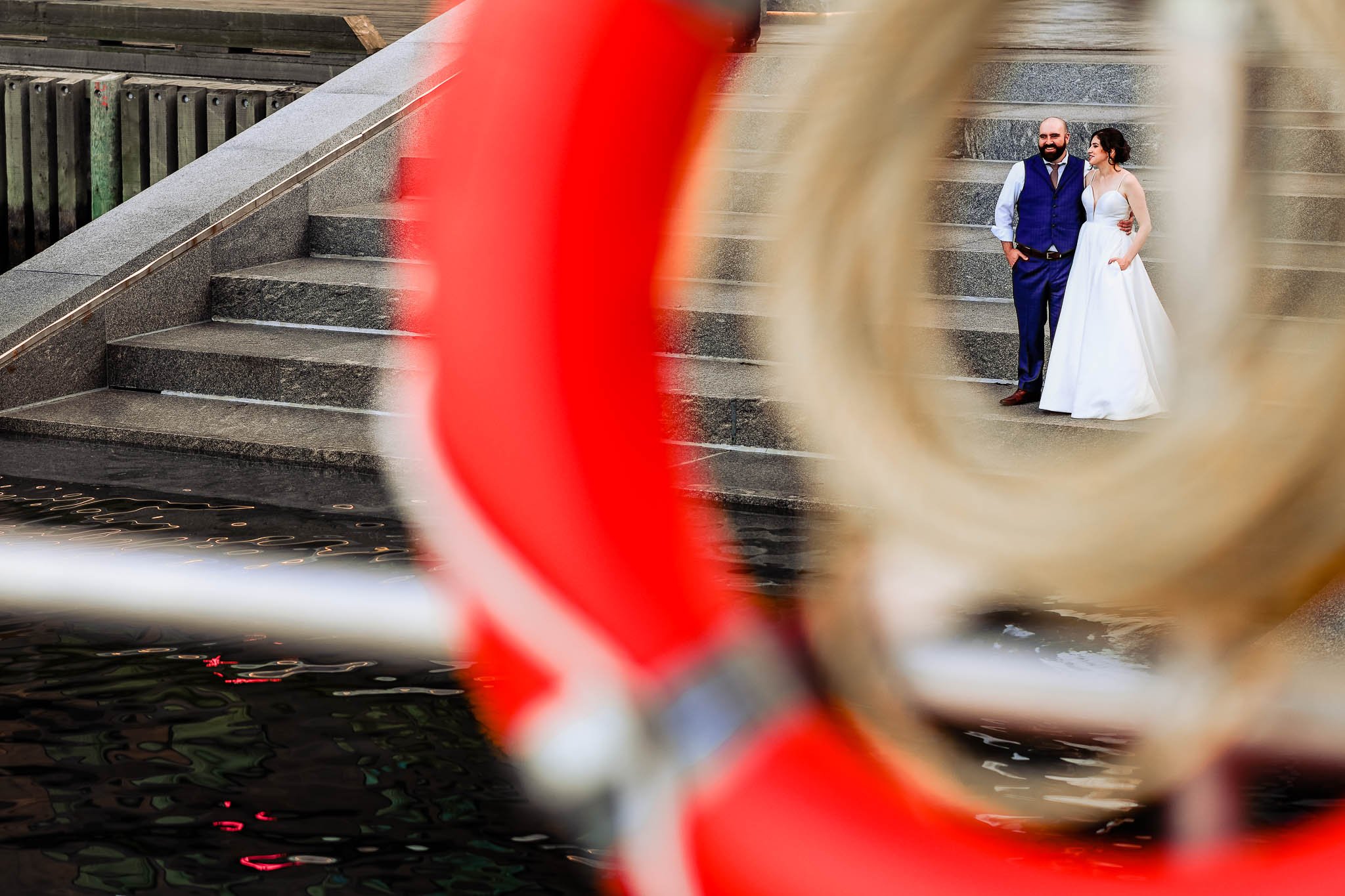 halifax waterfront with bride and groom standing on steps. image has orange lifesaver as a window to look through
