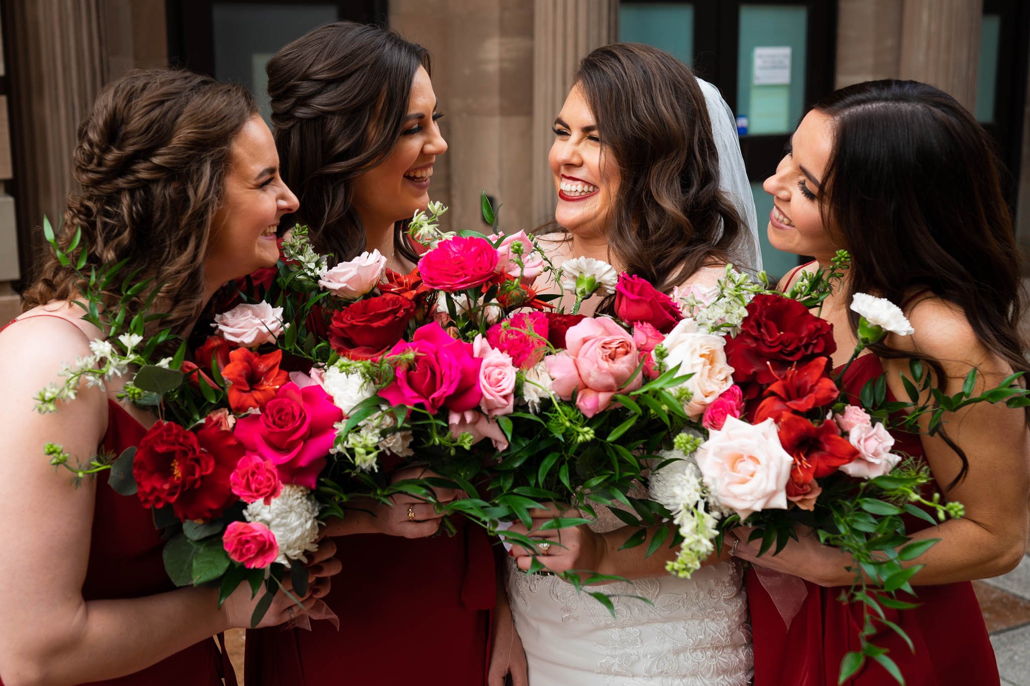 bride and bridesmaids laughing together holding bright pink and red boquets