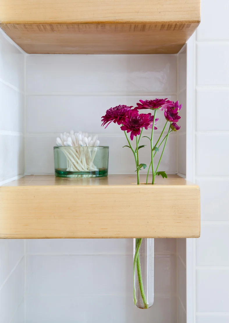Off-the-shelf glass containers are inset into wood shelves to allow for the orderly storage of bathroom supplies