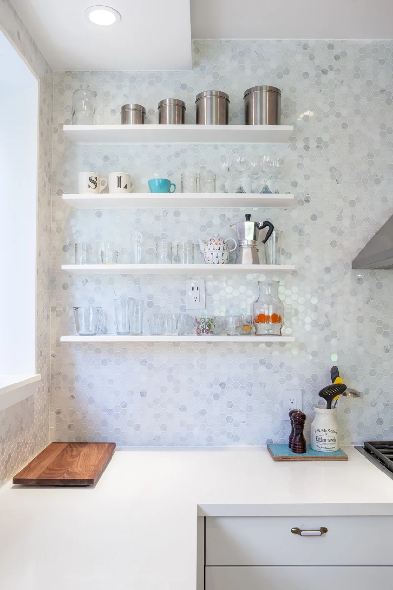 A hexagonal mosaic tile backsplash sparkles with reflected light; along with vintage brass pulls, these details add a touch of antique history to the otherwise sleek and modern kitchen cabinetry.