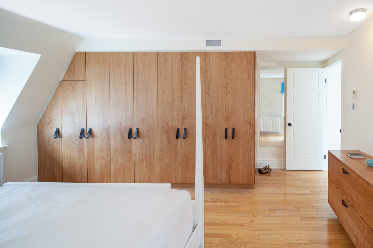 Custom cherry wardrobes detailed with leather pulls maximize available storage space under the angled ceiling of the third floor master bedroom. 