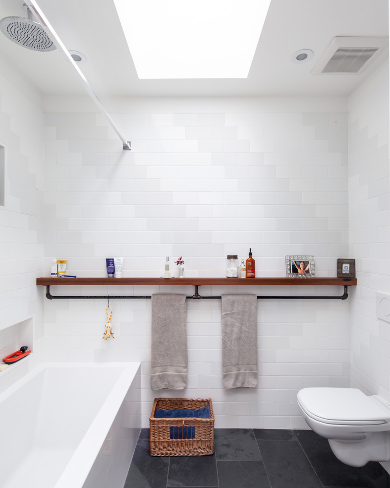 The bathroom is generously lit by natural light from two skylights above. A subtle but graphic pattern plays with the finish of standard white subway tile and wraps all sides of the ‘wet-room.’ A wall-hung toilet floats off the floor and makes for easy cleaning.