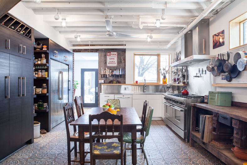 A modern plan combines the kitchen and dining areas into a large common room that is meant for cooking, entertaining and gathering. Double stoves with a stainless steel backsplash, the exposed joist ceiling, and open pegboard for storing cookware and utensils gives the kitchen an honest, utilitarian feel inspired by industrial kitchens.