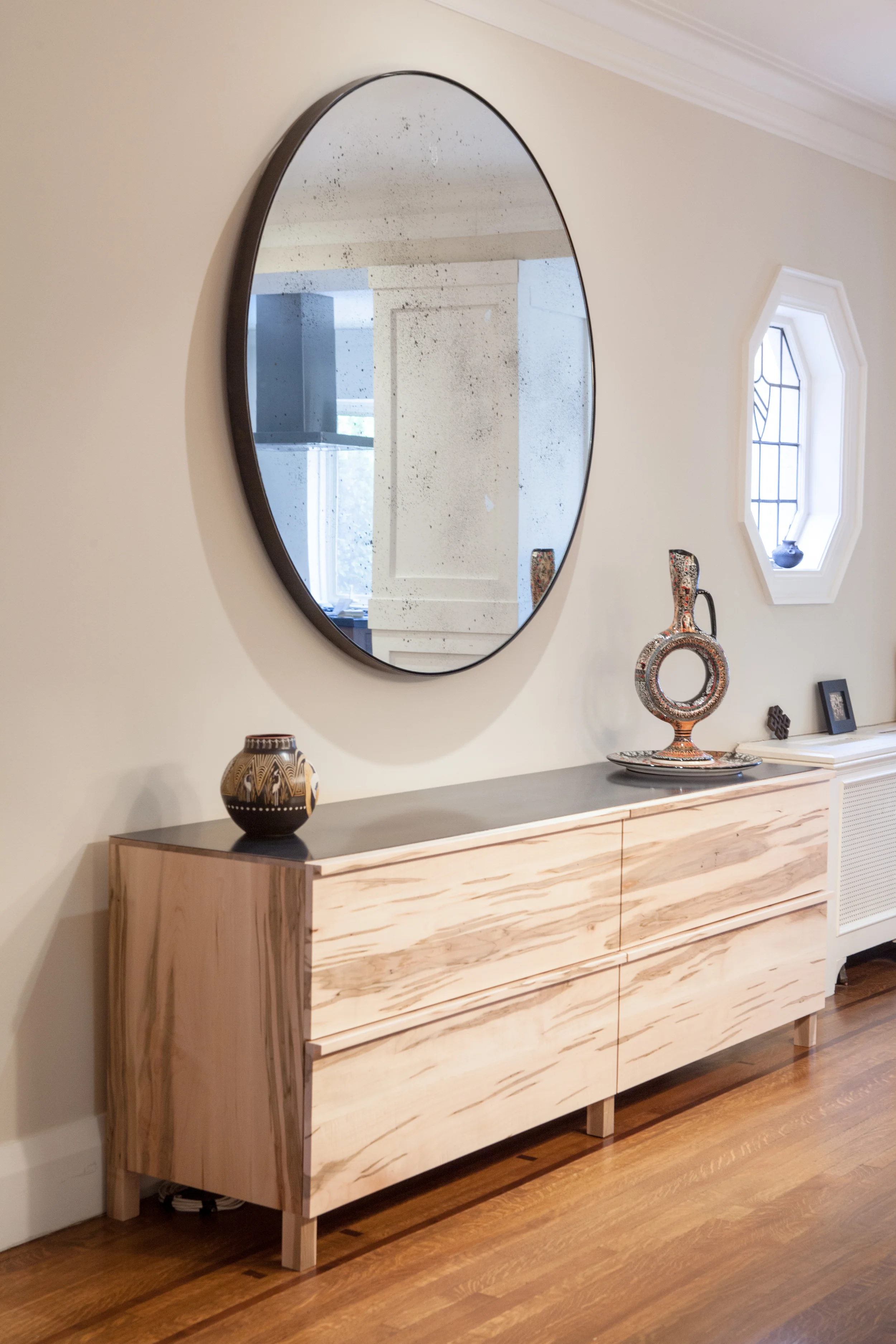 A custom built buffet and custom round antiqued mirror designed in collaboration with Commute Home (fabrication by Commute Home) provide an elegant backdrop for the family’s formal dining room. The thin black metal trim around the mirror echoes the top surface of the buffet and offsets the texture of the antiqued glass and pronounced grain of the maple buffet.