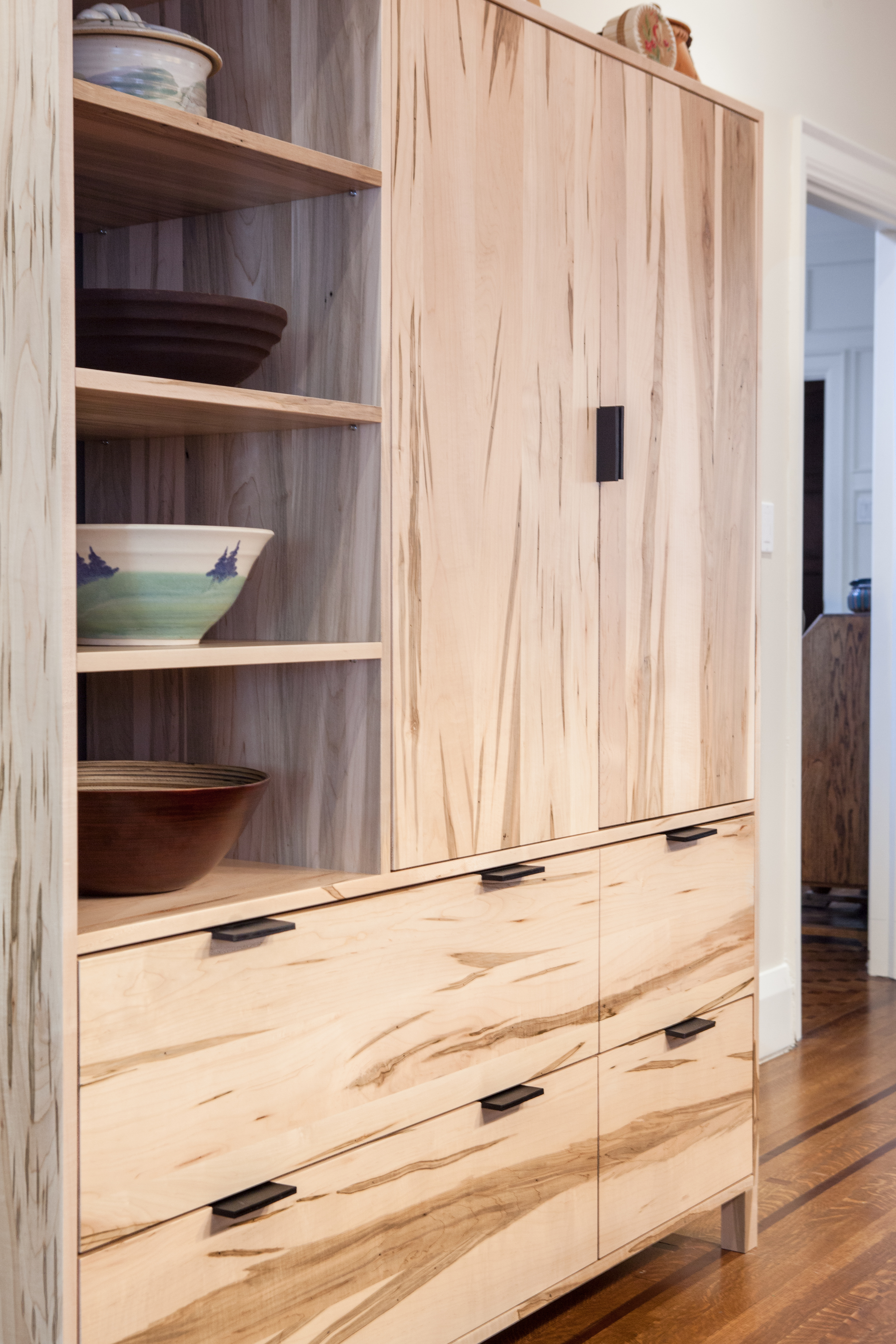 The texture and grain of spalted maple is showcased in this piece, designed in collaboration with Commute Home (fabrication by Commute Home). Open shelves display a variety of unique ceramic bowls.
