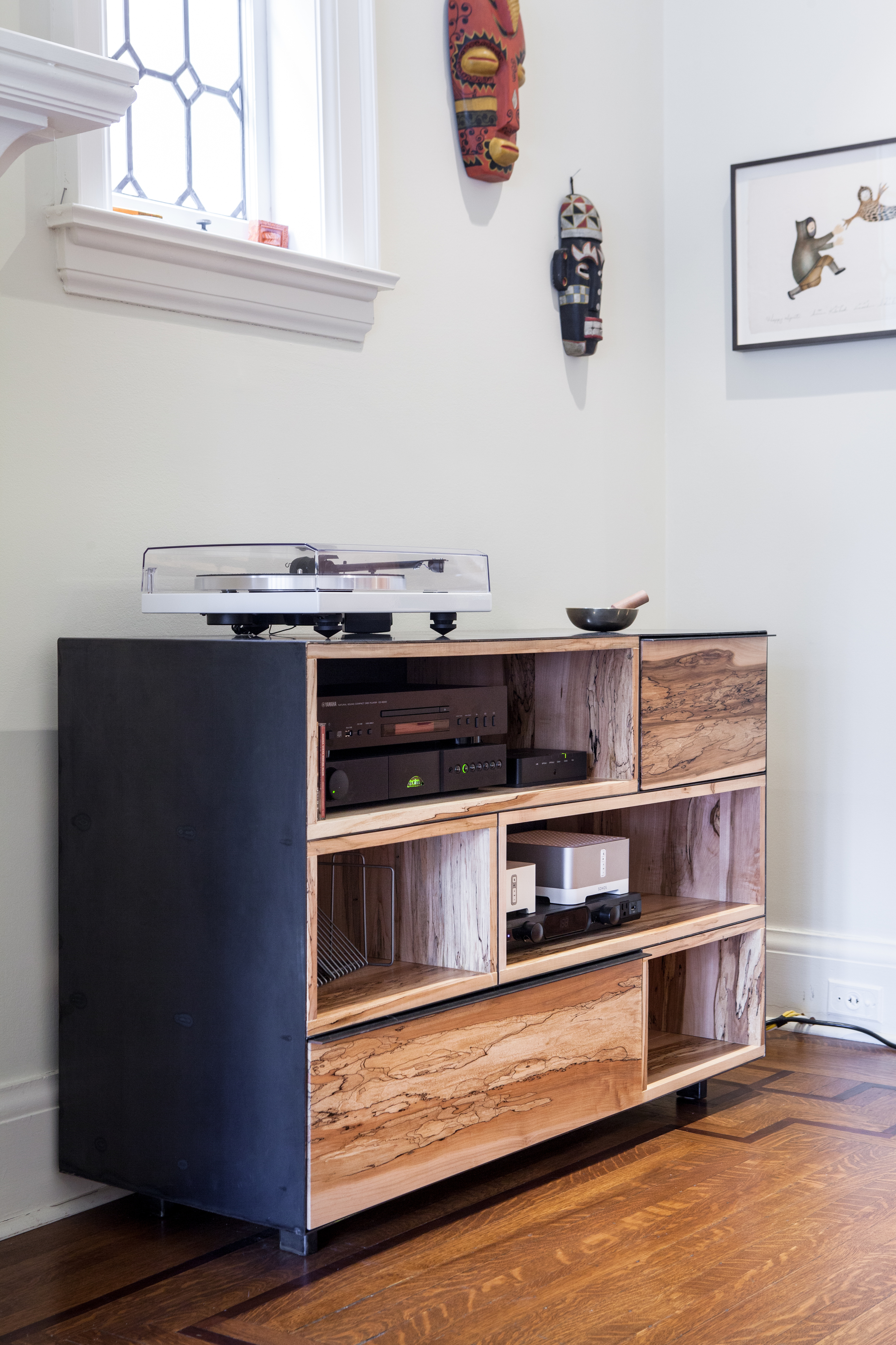 A metal wrapper envelopes the unit entirely, contrasting the warm texture of spalted maple.