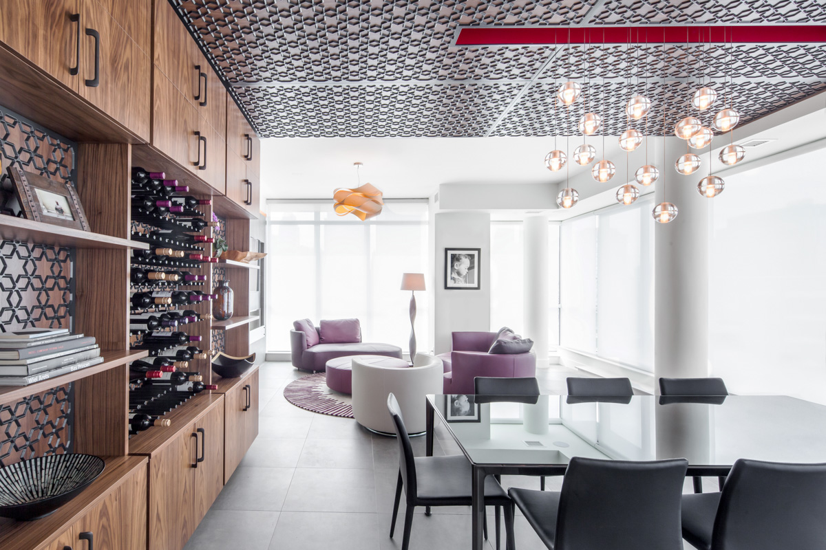 Upon entry to the main living space, the feature millwork frames a view to the living room beyond. A cascade of glass pendants hang effortlessly over the dining table, suspended from a vibrant red slot in the ceiling.