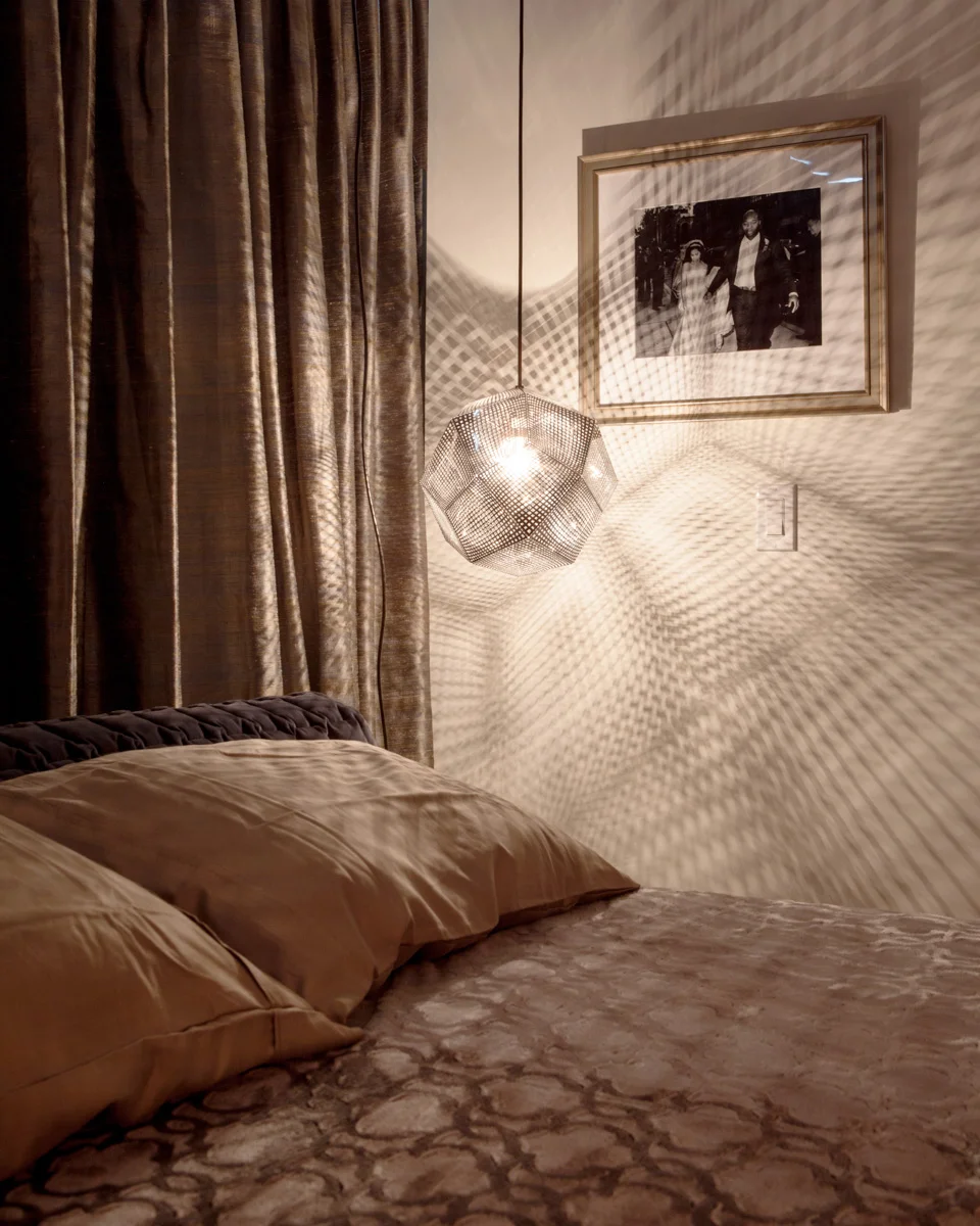 Bedside pendant lights sparkle and glow near the headboard, casting a dazzling geometry of warm shadows around the room.
