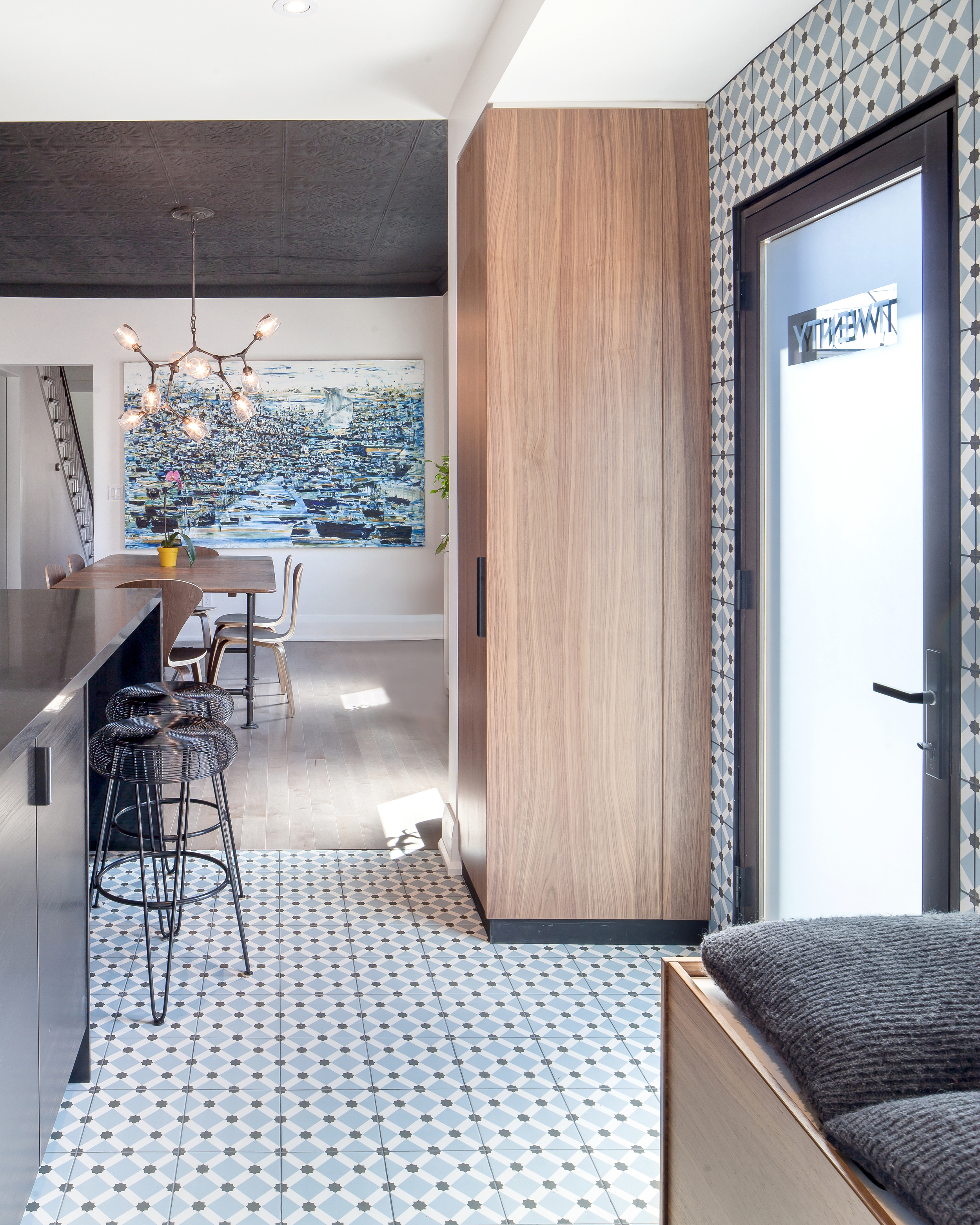 The side door is reimagined to become the family’s everyday entrance; a blue patterned tile wraps up the wall, defining a ‘mud room’ zone within the kitchen, with walnut closets on either side. The couple collaborated with a local typographic artist to design the custom text applied to the glass door.